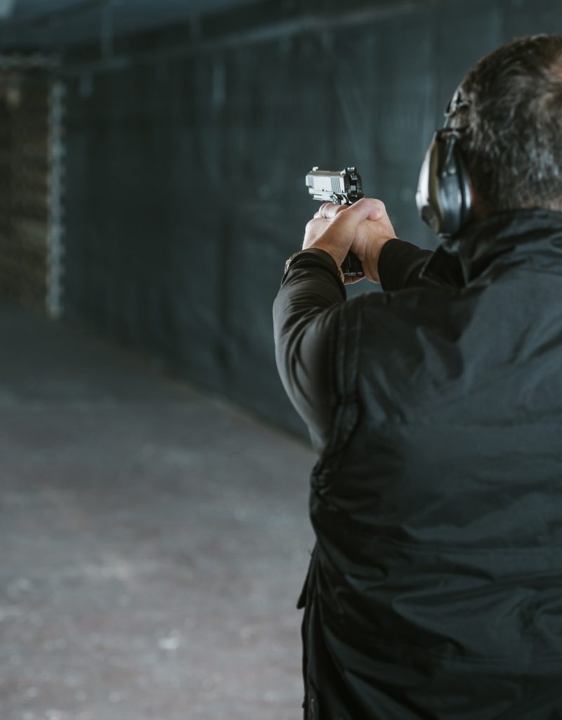 rear-view-of-man-aiming-gun-at-target-in-shooting-range.jpg